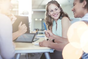 A businesswoman smiling while discussing notes with a colleague at a desk